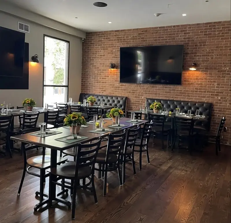 The back room set for a party: long tables, brick wall, leather banquettes and sunflowers.