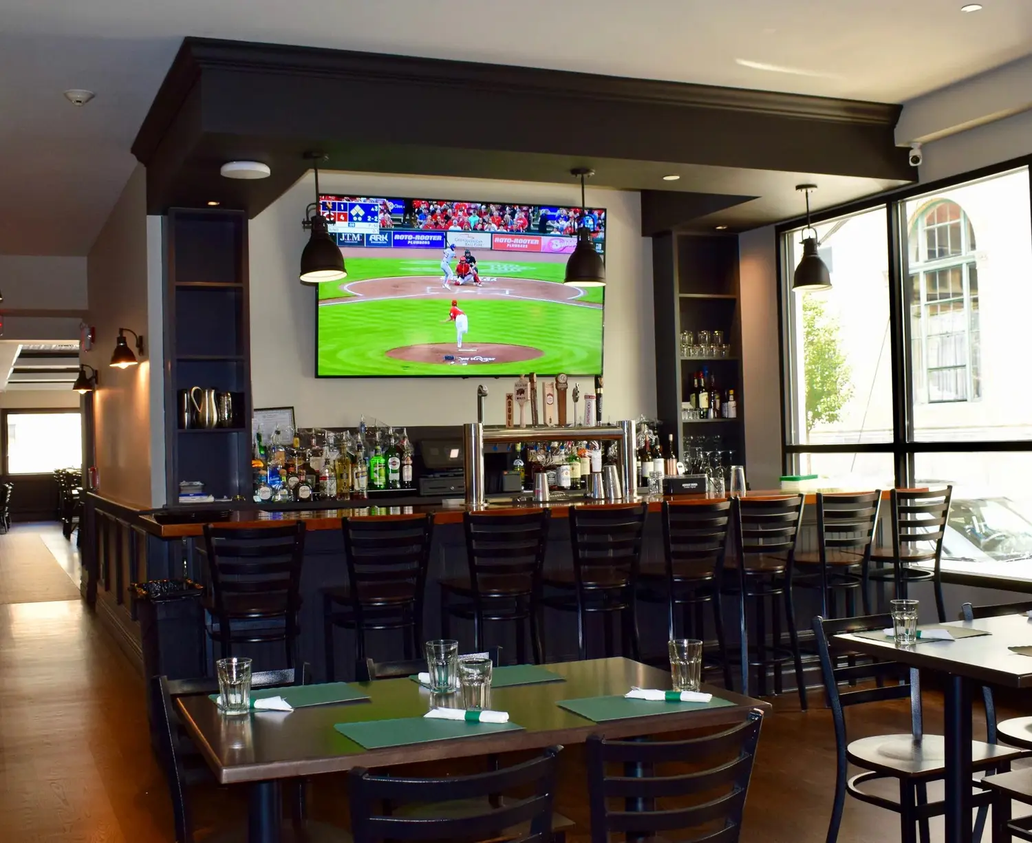 The bar room with a ballgame on the big screen and stools along the bar.