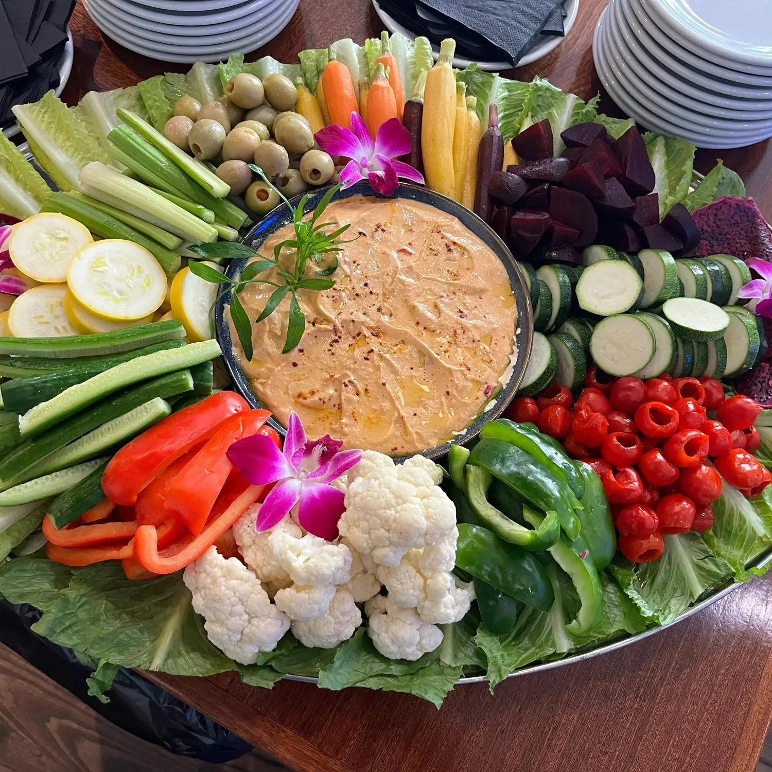 A large catering platter of fresh vegetables around a bowl of dip.