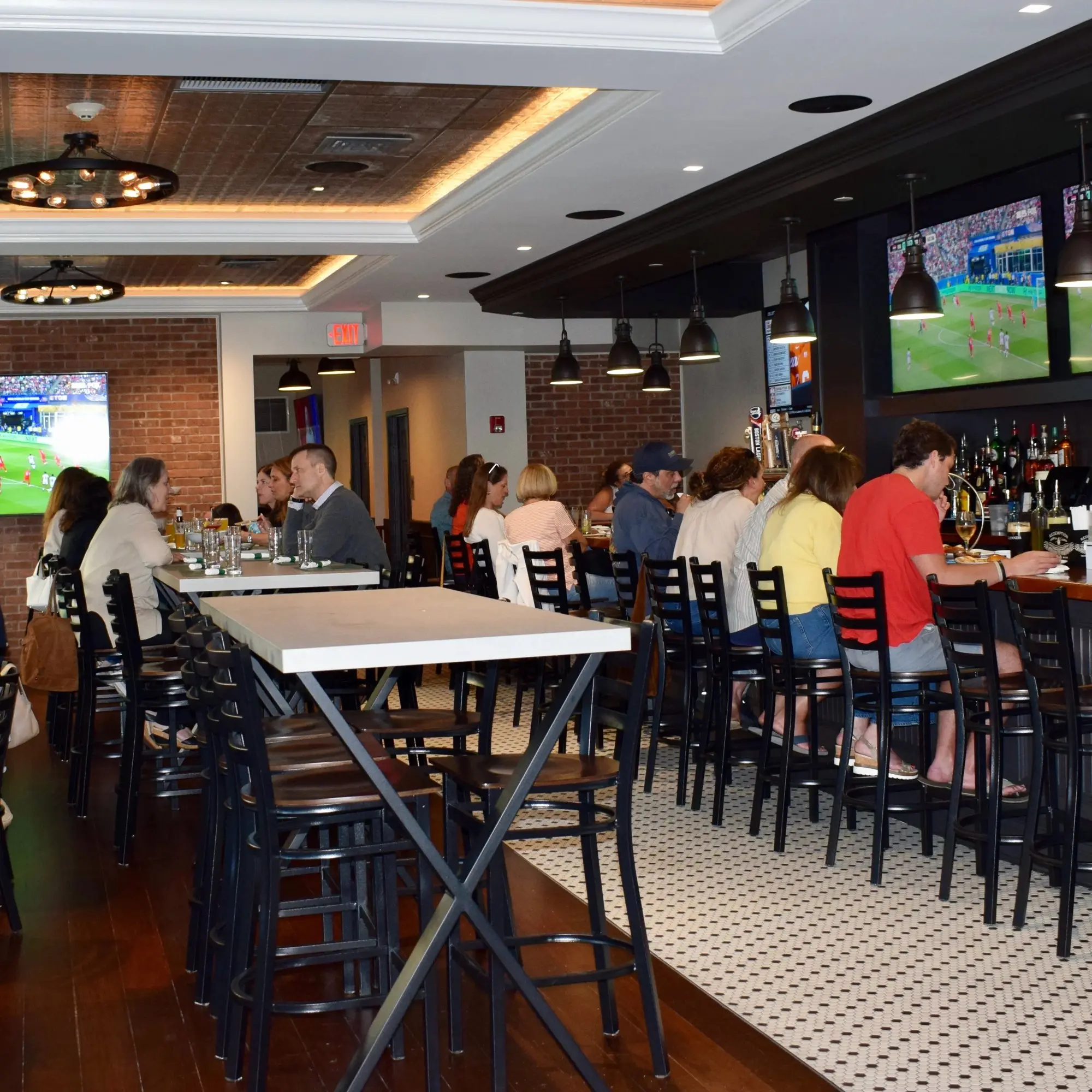 Guests at the bar and high-top tables, with games on the TVs.